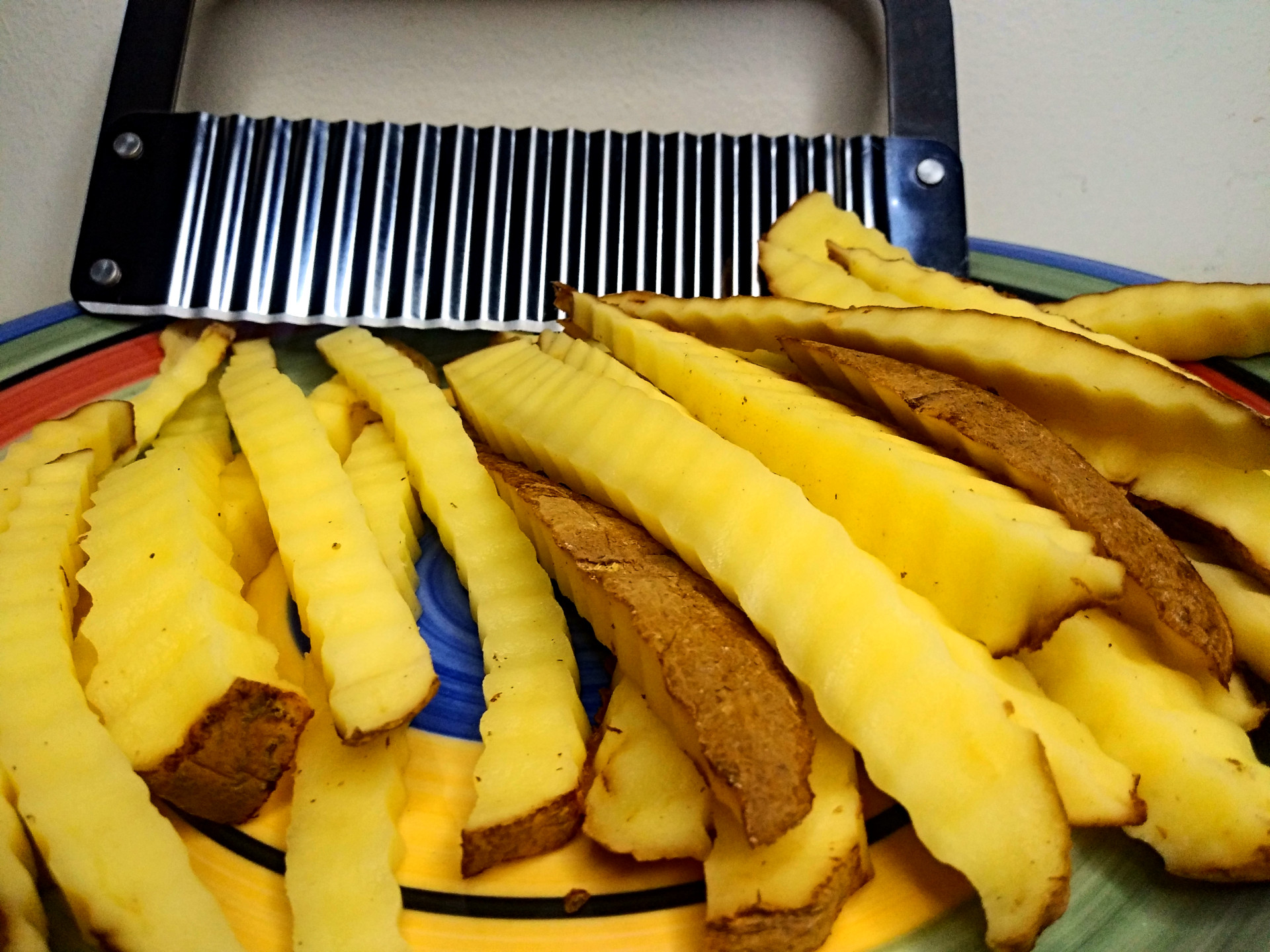 Plate of freshly crinkle cut fries on colorful plate with crinkle cutter visible at back of plate